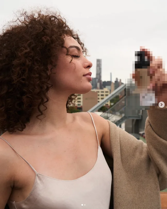 bareMinerals campaign still: model in profile on a rooftop holding a product bottle, city skyline behind her