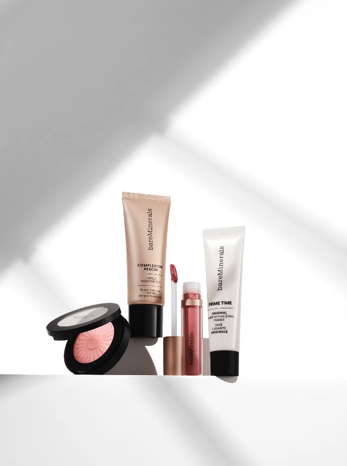 bareMinerals product shot: primer, foundation, blush and lip gloss on a white ledge in sunlight