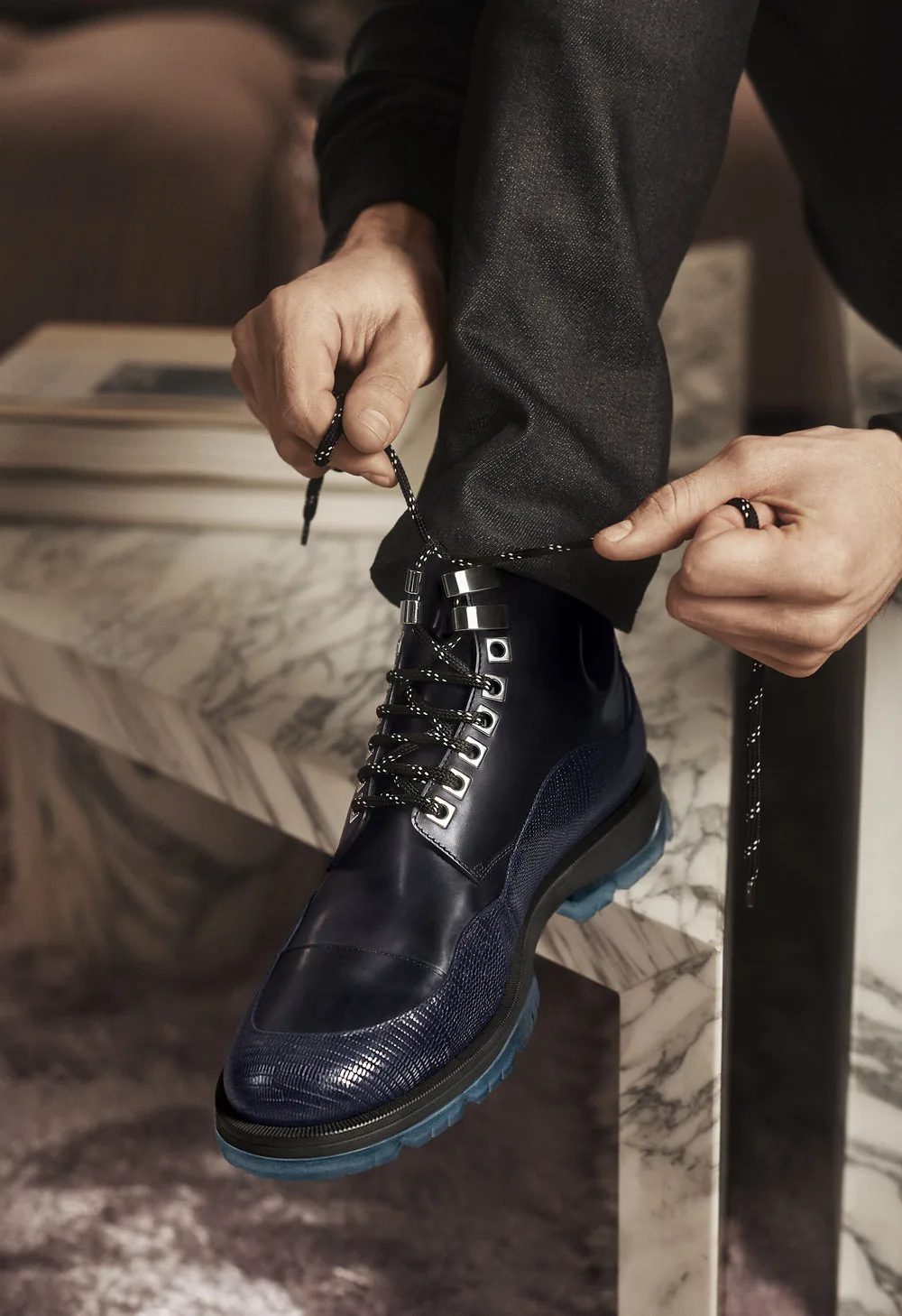 Jimmy Choo FW18 campaign still: a man laces a navy leather boot on a marble step, by Lachlan Bailey