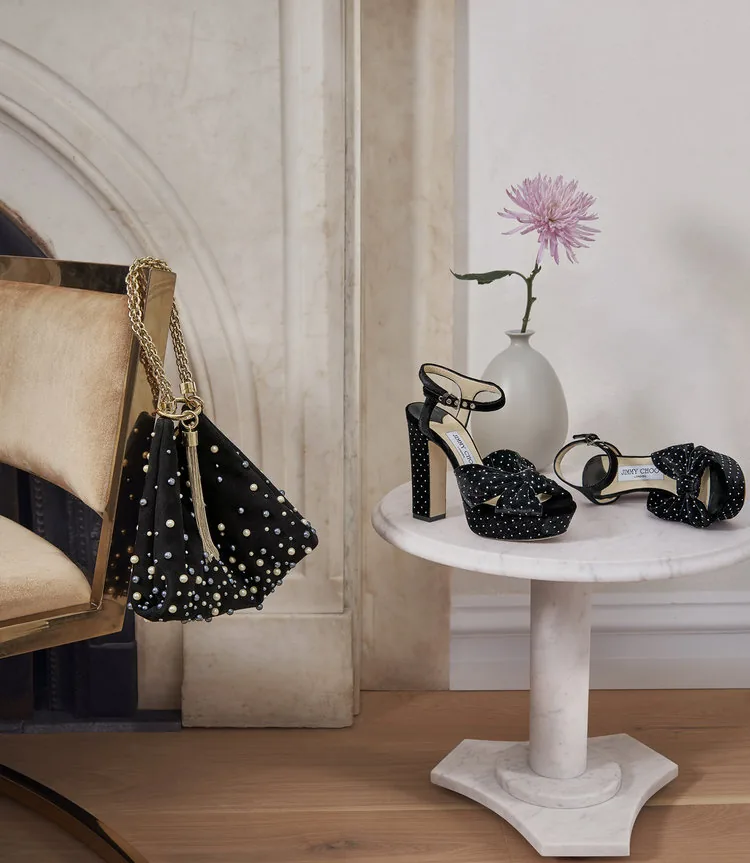 Jimmy Choo FW18 still life: studded black sandals on a marble pedestal beside a pink flower, by Maxime Poiblanc