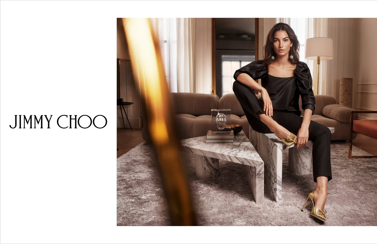 Jimmy Choo FW18 print ad layout: Lily Aldridge on a marble table in gold heels, with the wordmark