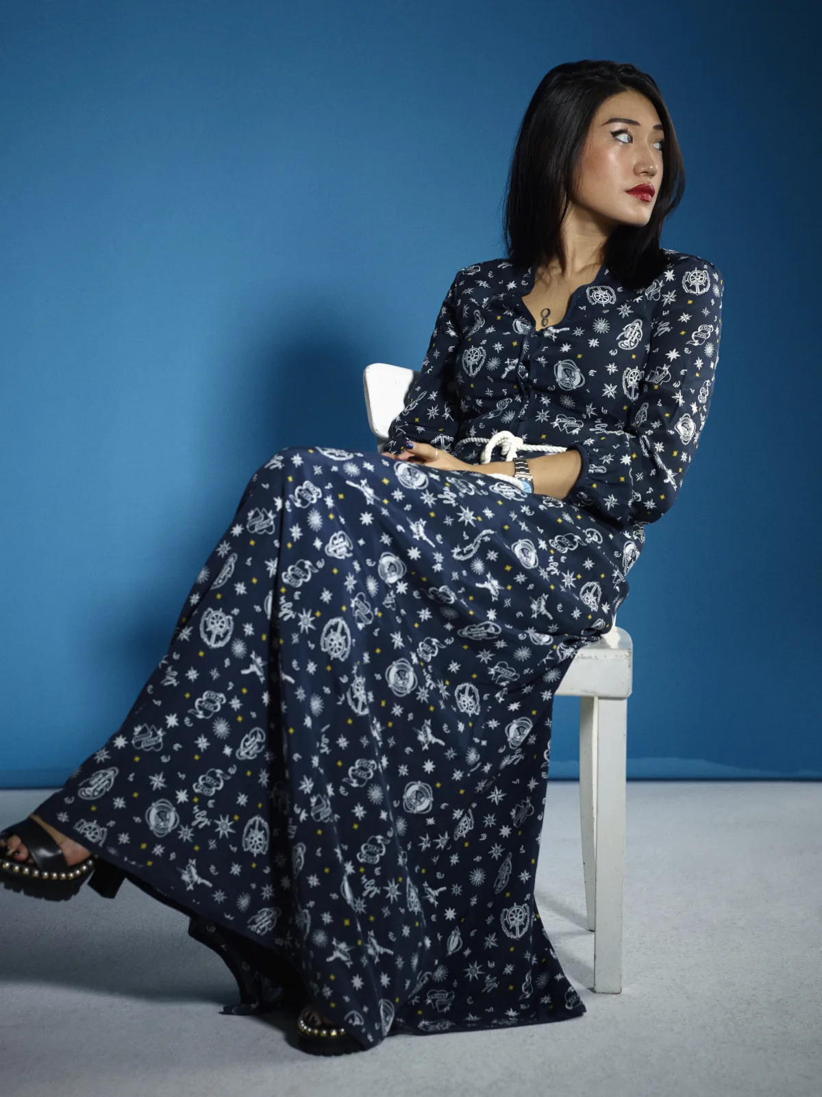 Influencer in a navy printed maxi dress seated on a white chair against a blue backdrop, Berlin