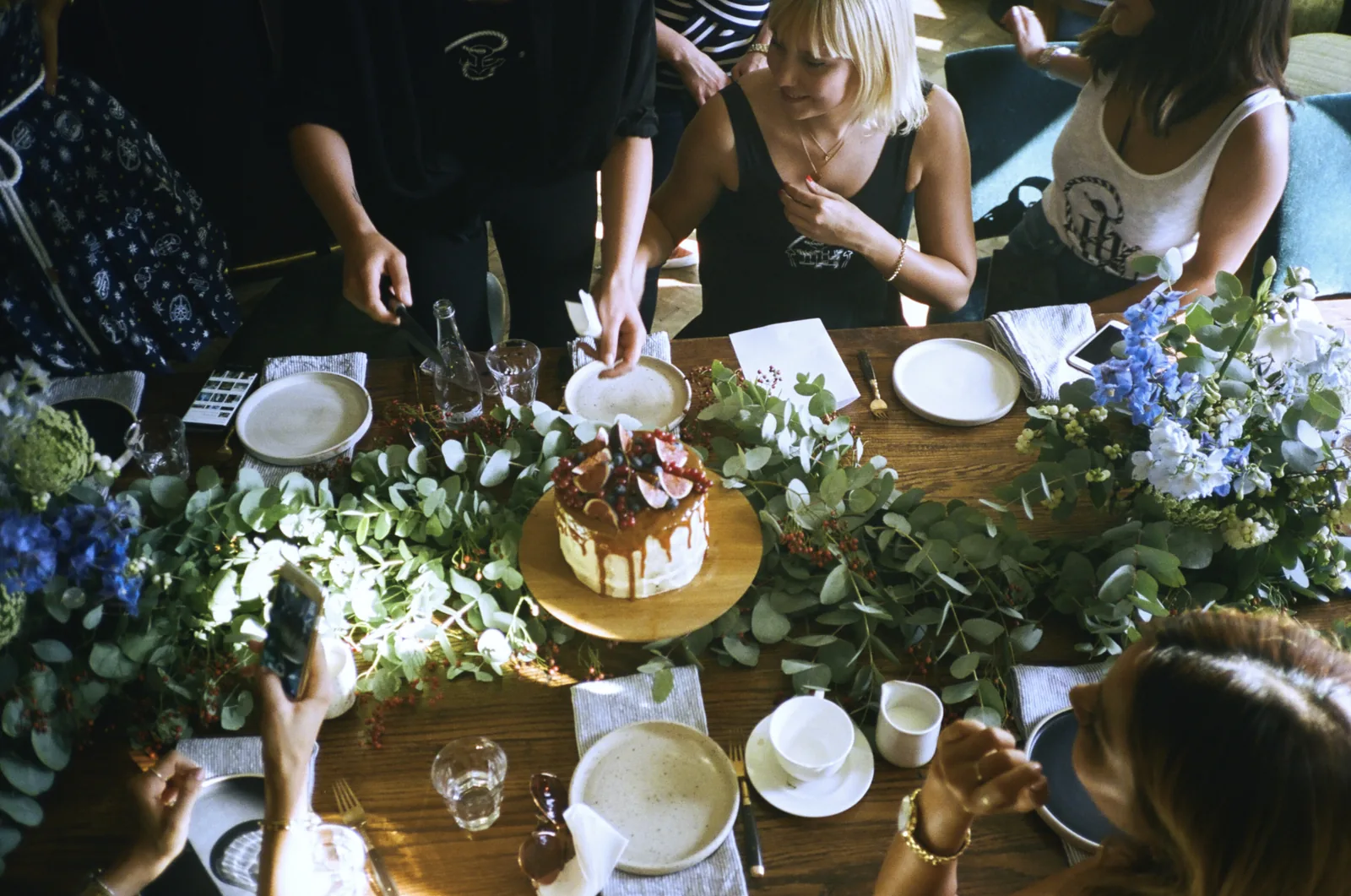 Overhead view of guests photographing a cake on a flower-decked table at the Tommy x Gigi dinner, Berlin
