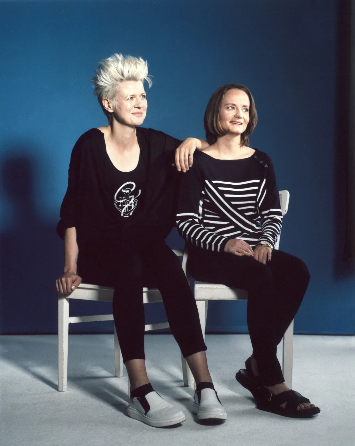 Two influencers in navy and striped Tommy x Gigi knits share a white chair against a blue backdrop