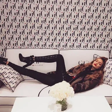 Gigi Hadid reclines on a white sofa against Gigi-patterned wallpaper, tour social post