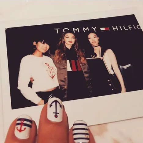 Polaroid of Gigi Hadid with two fans at a Tommy Hilfiger backdrop, held by a hand with nautical nail art
