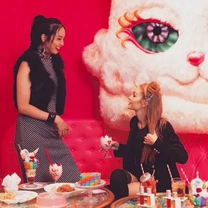Gigi Hadid in a pink cafe beside a giant plush cat and colorful desserts, Tommy x Gigi tour, Tokyo