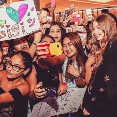 Gigi Hadid among a crowd of fans holding phones and I love Gigi signs