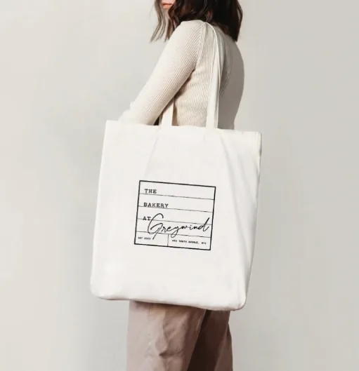 Woman carrying a white tote bag printed with The Bakery at Greywind