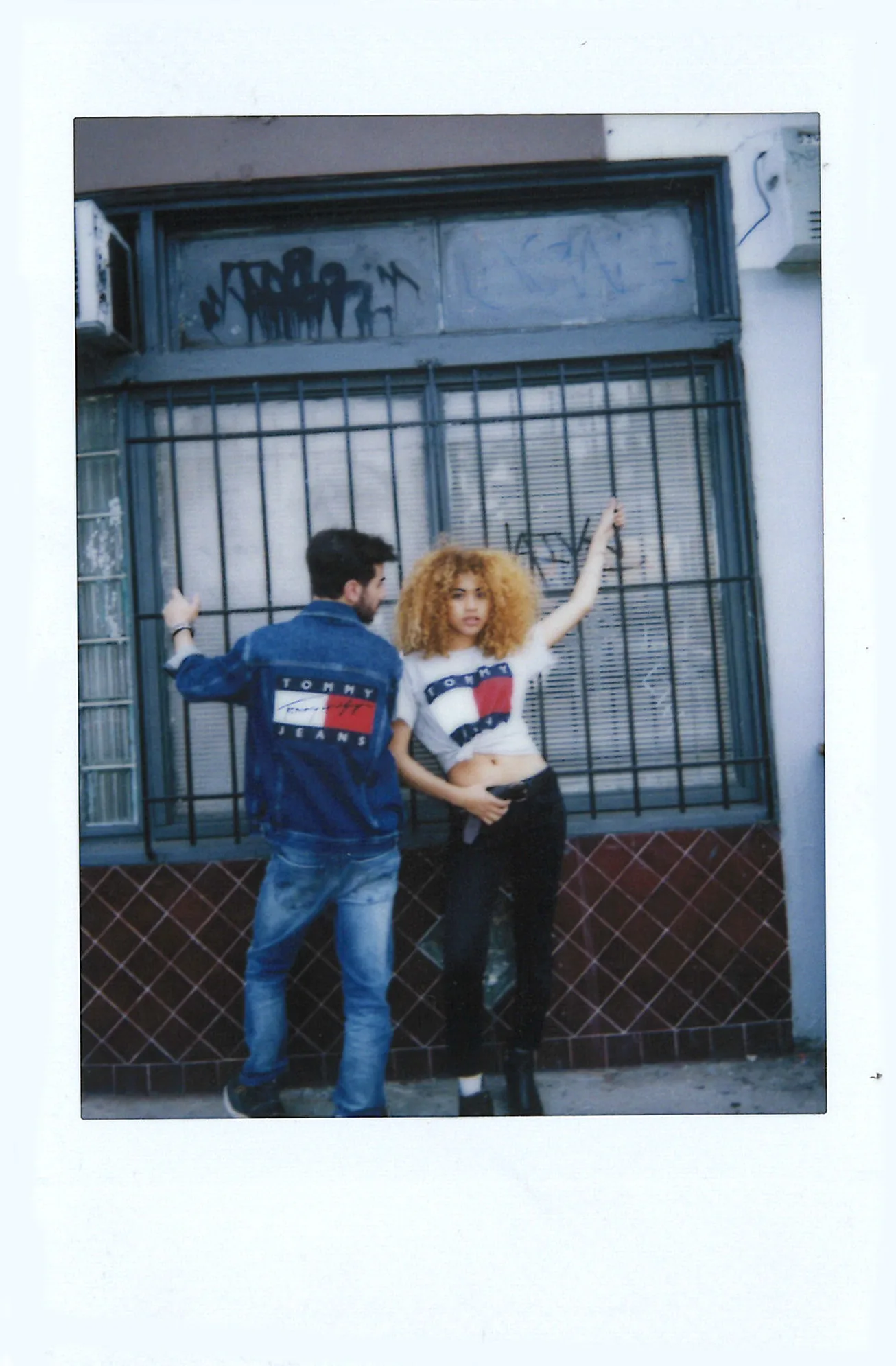 Polaroid of a couple in Tommy Jeans posing in front of a shop window