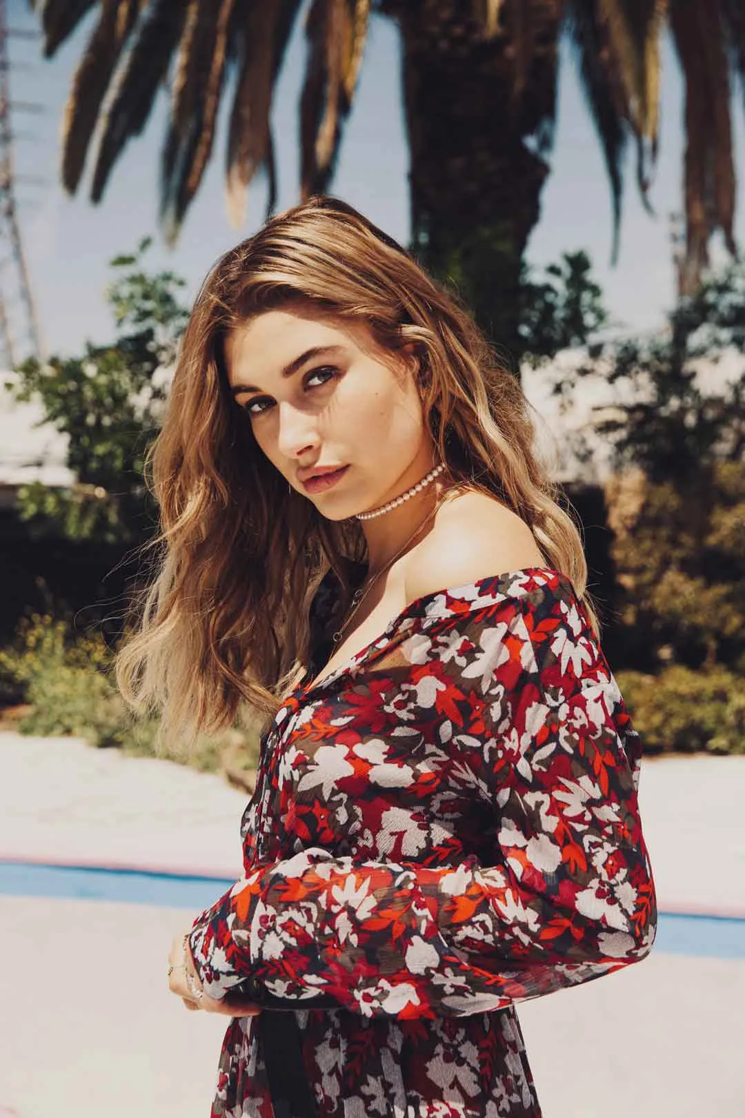 Woman with long hair in a red floral dress under palm trees, shot by Bryant Eslava
