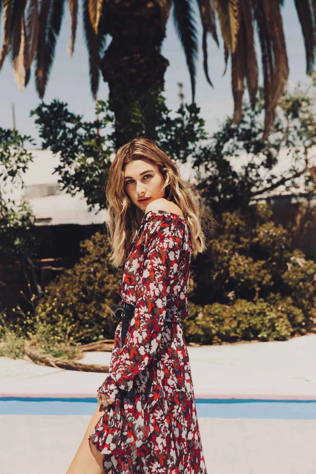 Woman in a red floral dress standing beside an empty pool under palm trees, shot by Bryant Eslava