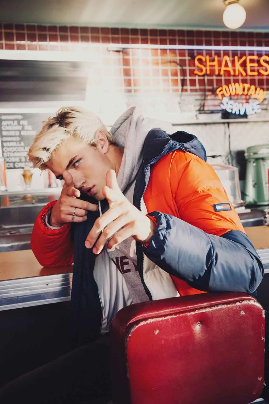 Lucky Blue Smith in a puffer jacket in a diner booth under a Shakes neon sign, shot by Bryant Eslava