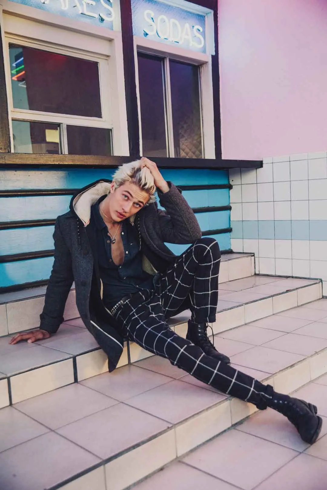 Lucky Blue Smith reclining on tiled steps in checked trousers, shot by Bryant Eslava