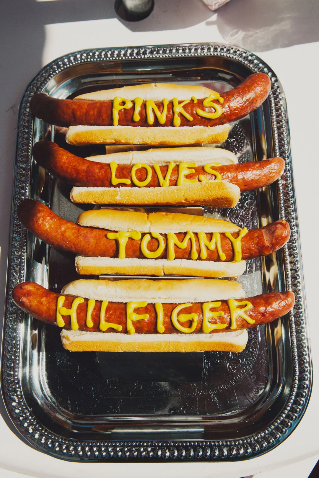 Tray of hot dogs with Pink's loves Tommy Hilfiger written in mustard, shot by Bryant Eslava