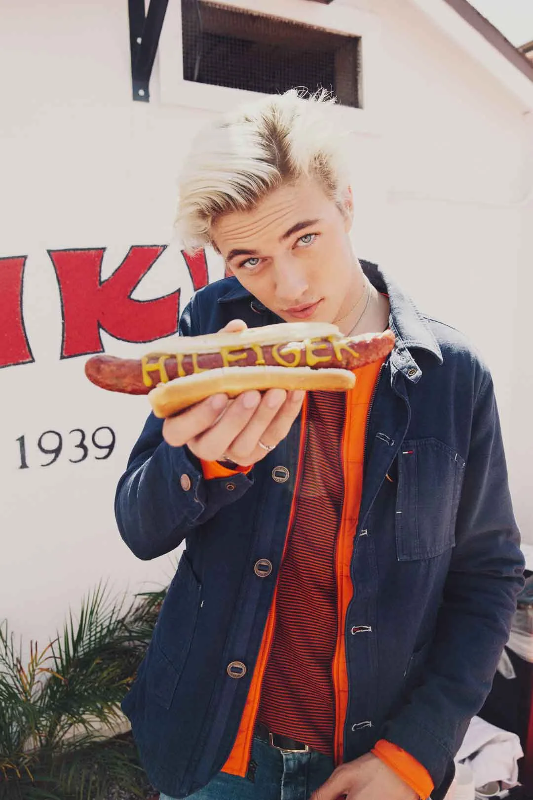 Lucky Blue Smith holding a hot dog lettered Hilfiger in mustard outside Pink's, shot by Bryant Eslava