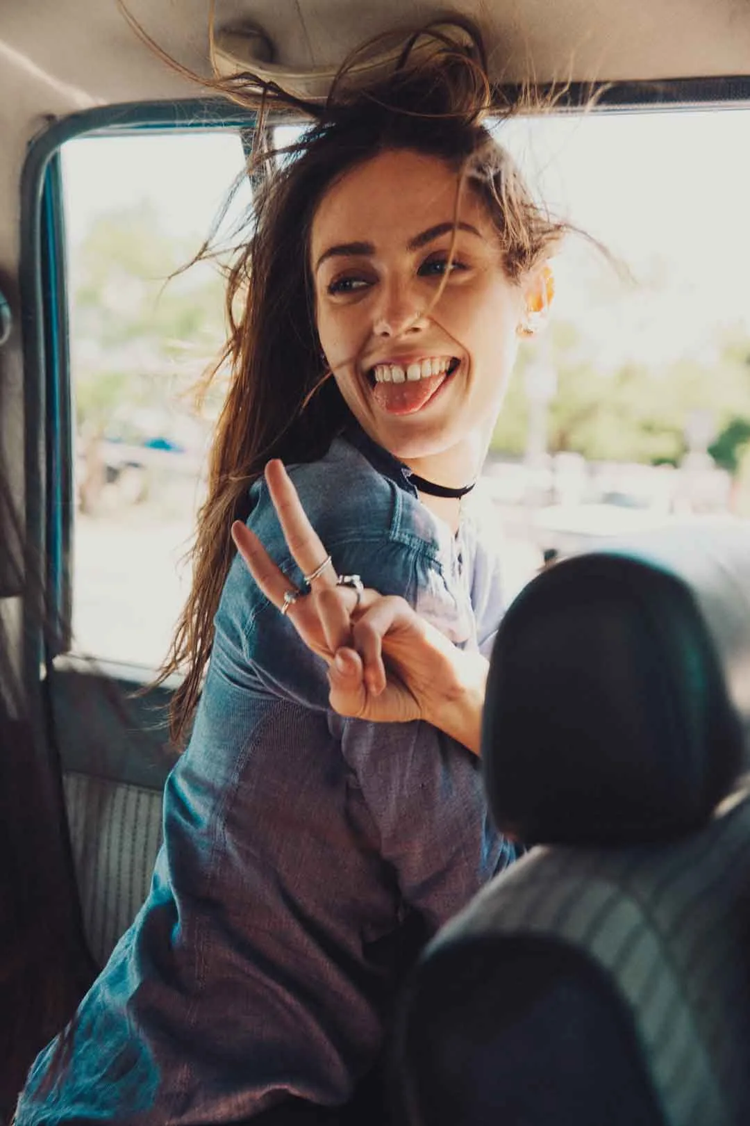 Woman flashing a peace sign with her tongue out in the back of a car, shot by Bryant Eslava