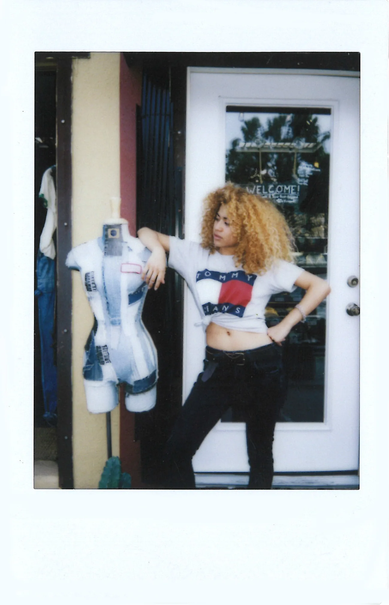 Polaroid of a curly-haired woman in a Tommy Jeans tee beside a mannequin outside a shop