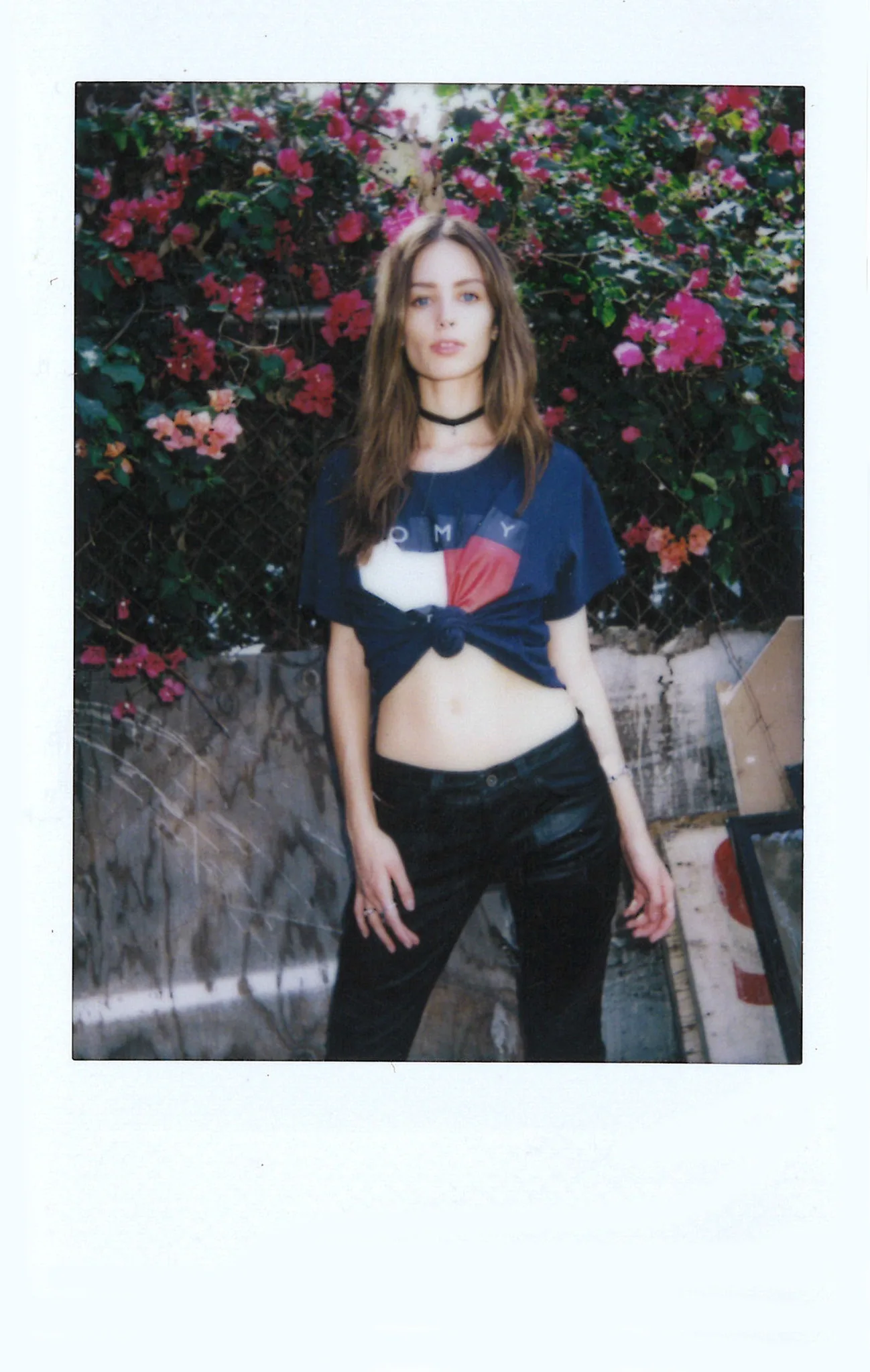 Polaroid of a woman in a knotted Tommy Jeans tee standing in front of bougainvillea