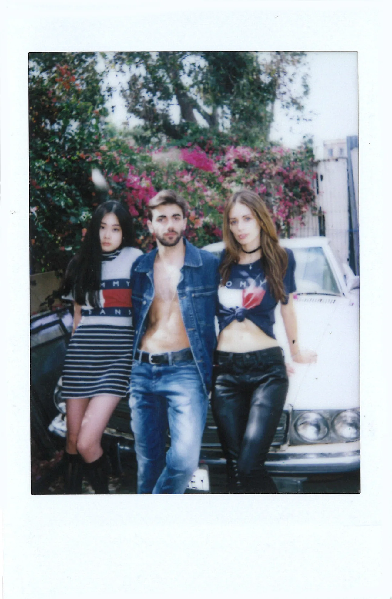 Polaroid of three friends in Tommy Jeans leaning on a car under bougainvillea