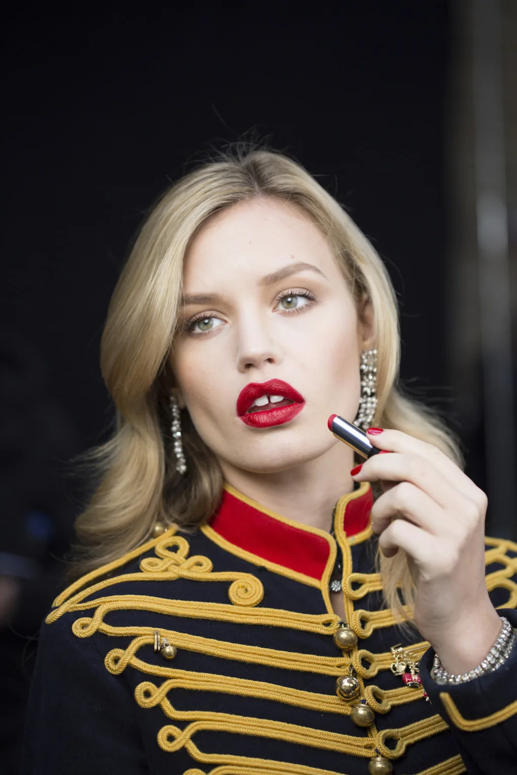 Georgia May Jagger in a gold-braided military jacket holding a red Rimmel lipstick