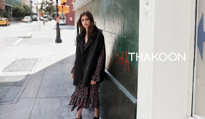 Thakoon Fall 16 campaign still: model in a black coat over a floral dress against a green wall