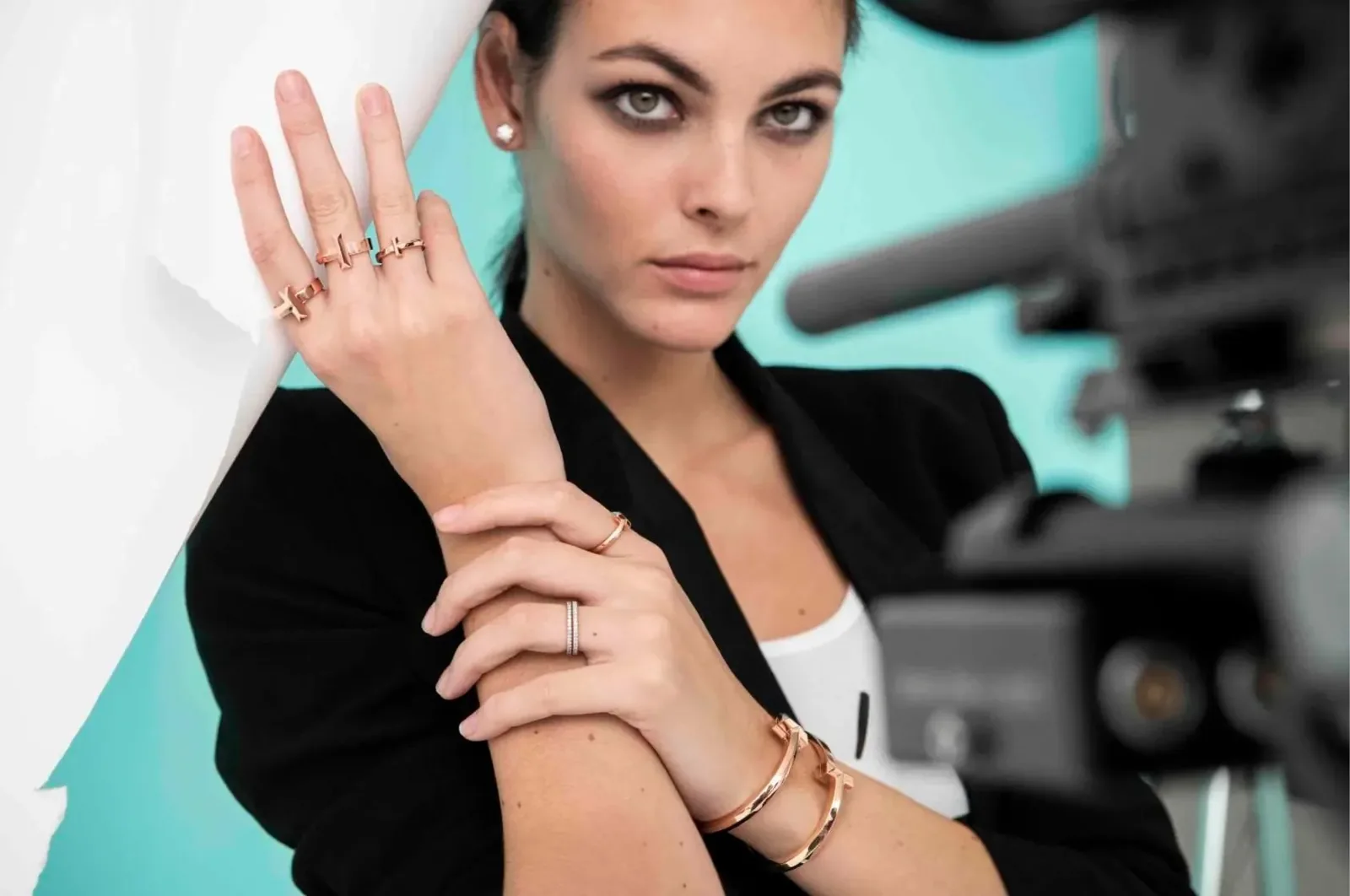 Vittoria Ceretti in a black blazer showing Tiffany T1 rose-gold bracelets and rings, behind the scenes with a camera
