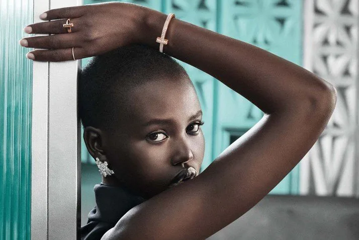 Adut Akech with an arm over her head wearing a Tiffany T1 ring and bracelet against a Tiffany blue wall