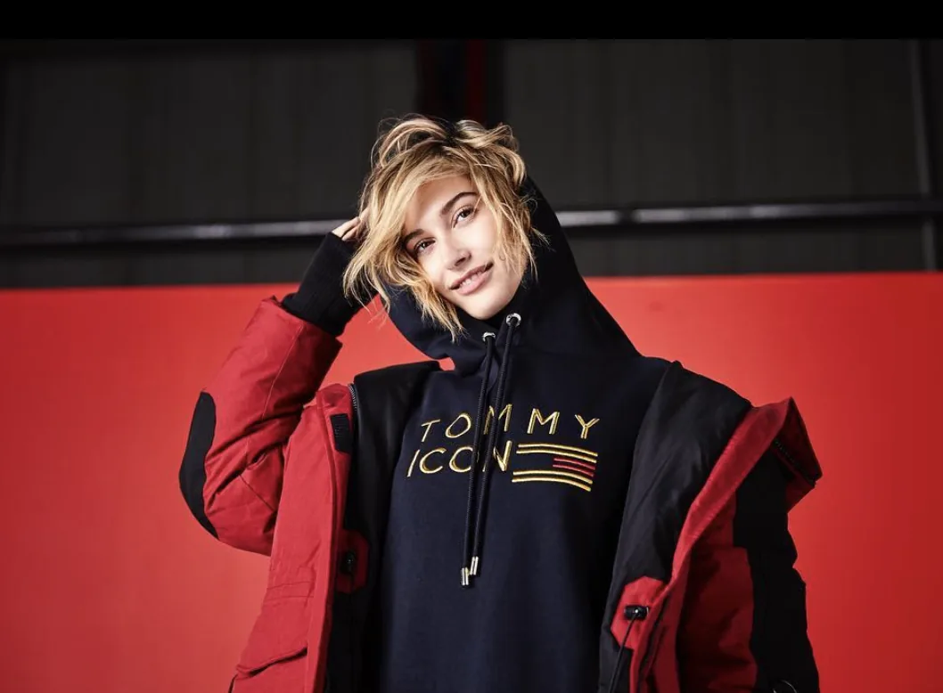 Tommy Icons campaign still: Hailey Baldwin in a Tommy Icon hoodie and red parka against a red backdrop