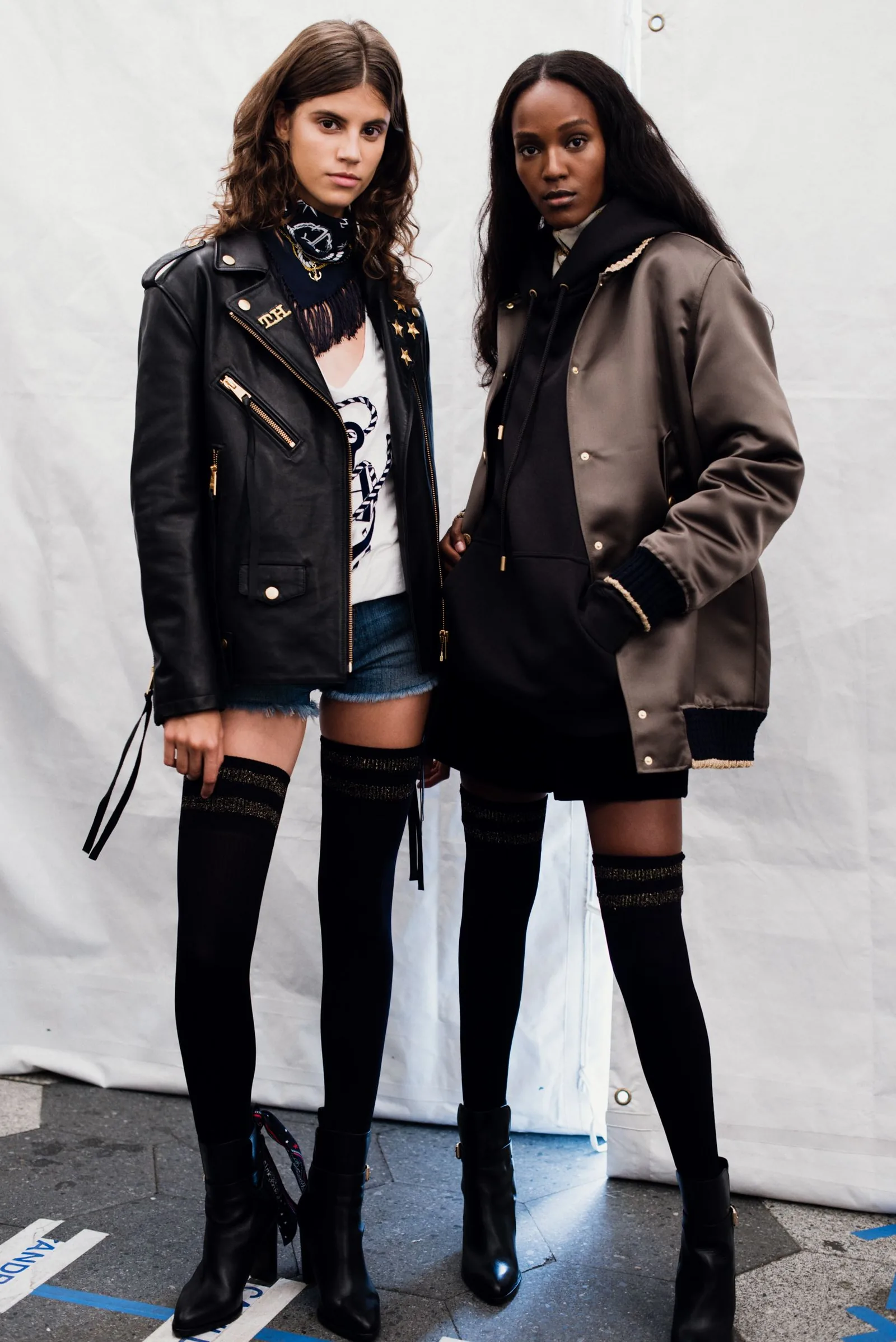 TommyNow backstage: two models in leather and bomber jackets with thigh-high socks