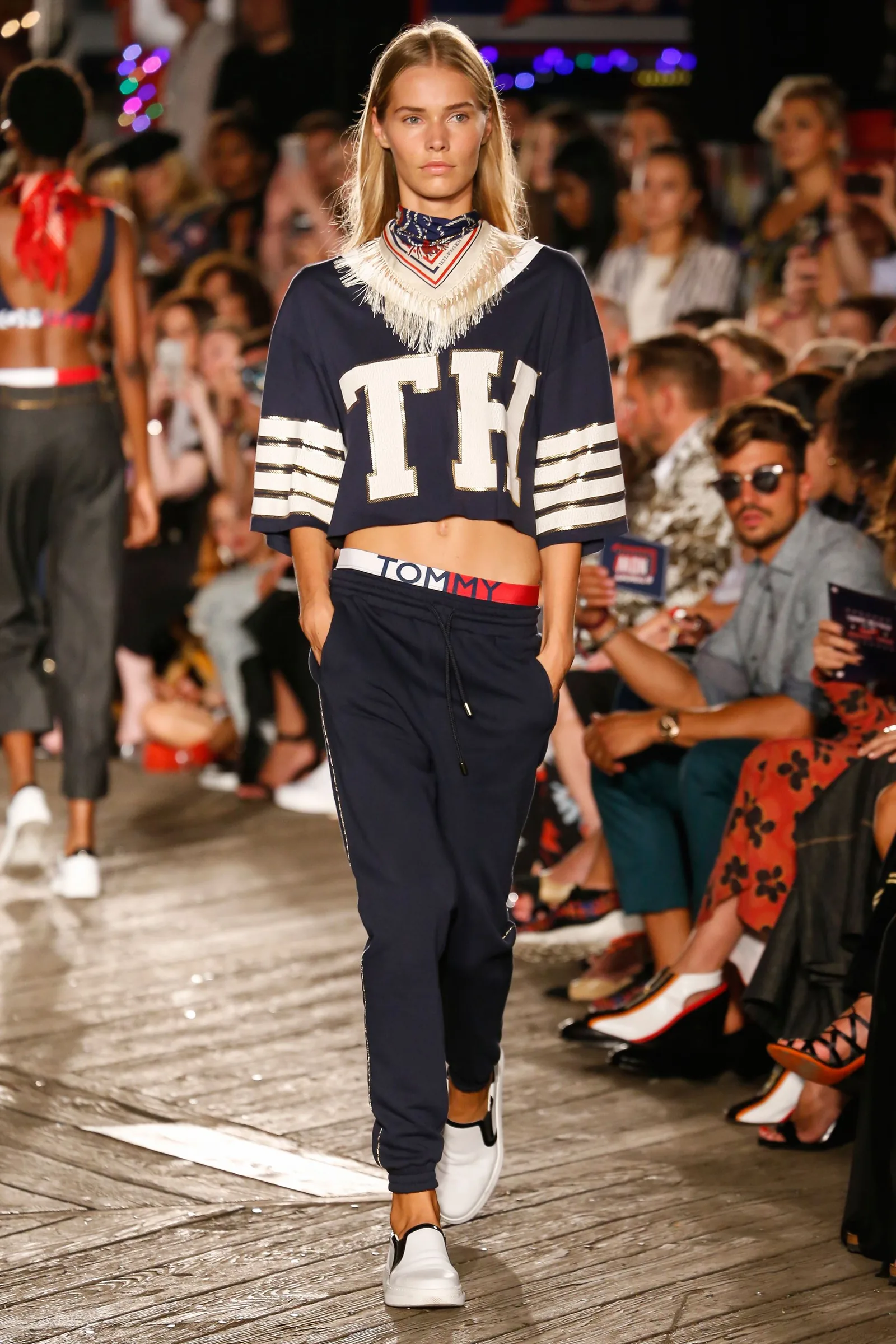 TommyNow runway look: a model in a cropped TH varsity top and navy track pants
